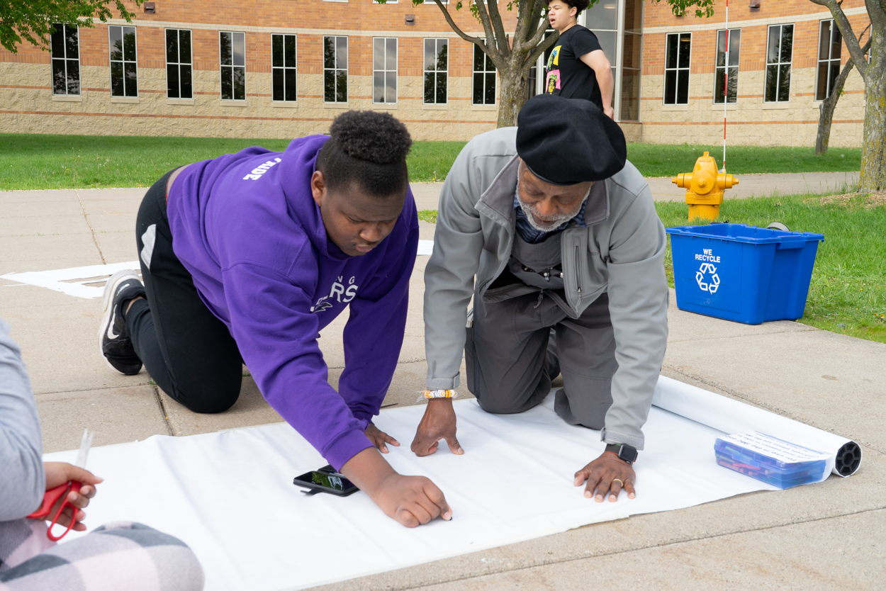 Artist Seitu Jones works with a member of the Red Wing High School Black Student Union to trace shadows on the sidewalk.