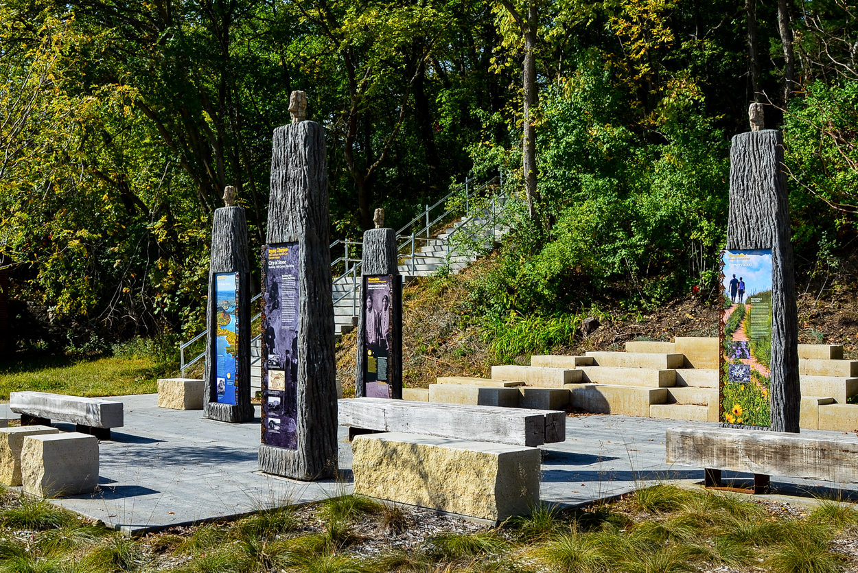large, figure-like columns support interpretive signage in an outdoor park with limestone seating.