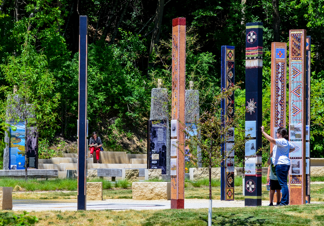 Tall, thin, colorful posts arranged in a circle display images and text at the He Min Can Trailhead.
