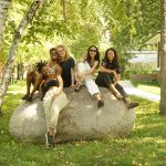 Five people sit on a large boulder in the Anderson Center Sculpture Garden.