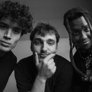 Black and white photo of three young jazz musicians leaning in towards the camera.